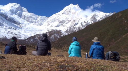 Scenic view of the 7-day Short Manaslu Trek route in Nepal, showing snow-capped mountains, lush green valleys, traditional Himalayan villages, and trekkers walking along a narrow trail under clear blue skies.