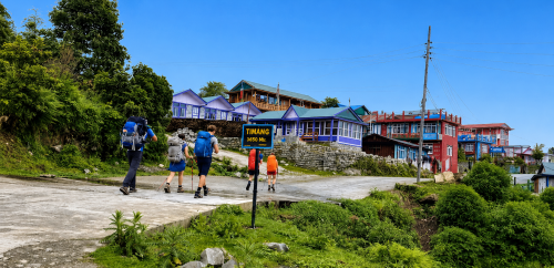 Trekkers walking through Timang village on the Annapurna Circuit Trek beneath clear blue skies and lush hills.