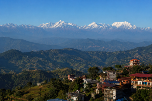 Panoramic view from Nagarkot, Nepal, showing snow-capped Himalayan peaks including the Langtang range, distant Everest region mountains, and Ganesh Himal, layered behind rolling green hills with terraced fields, scattered villages, and hillside hotels under a clear blue sky.