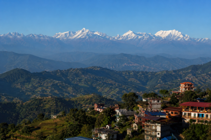 Panoramic view from Nagarkot, Nepal, showing snow-capped Himalayan peaks including the Langtang range, distant Everest region mountains, and Ganesh Himal, layered behind rolling green hills with terraced fields, scattered villages, and hillside hotels under a clear blue sky.