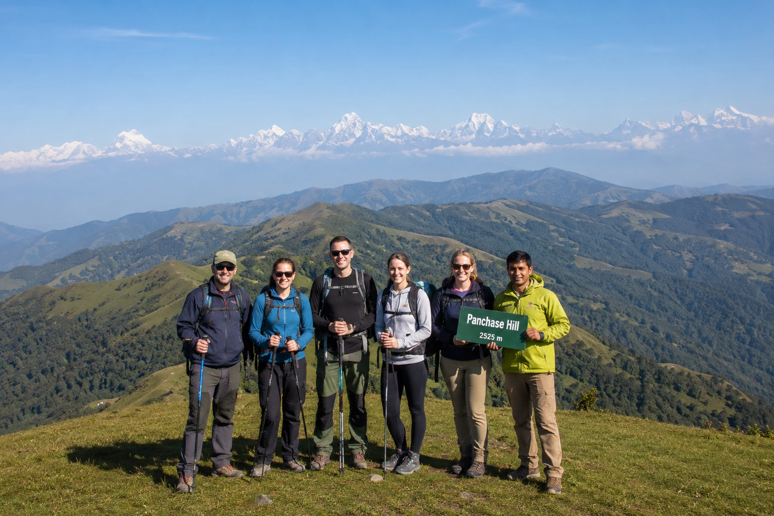Group of hikers with a local Nepali guide standing on the summit of Panchase Hill (2,500 m) near Pokhara, Nepal, surrounded by rolling green hills and panoramic Himalayan mountain views under a clear blue sky.