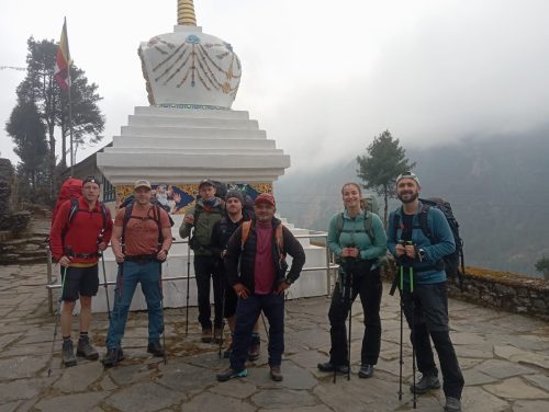 Trekkers crossing a high Himalayan pass in the Khumbu region with panoramic views of Mount Everest and surrounding snow-capped peaks under a clear sky.