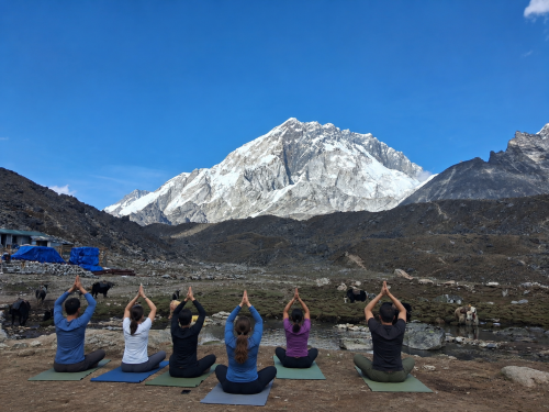 Trekkers practicing yoga during the Everest Base Camp Yoga & Meditation Trek with Mount Everest, Ama Dablam, and Himalayan peaks at sunrise.