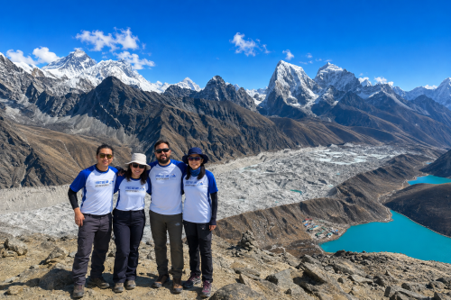 Trekkers overlooking stunning Gokyo Lakes surrounded by snowy Himalayan peaks under sunshine.
